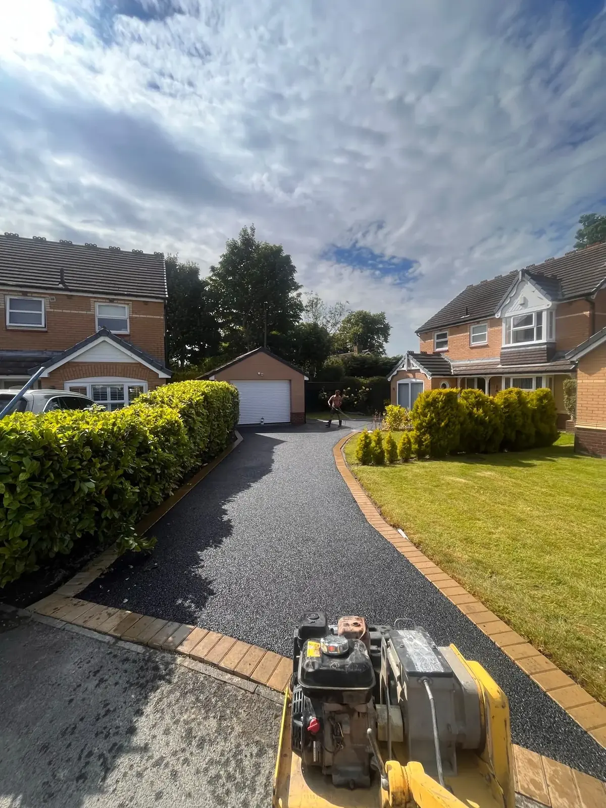 Long newly laid tarmac driveway running between hedges and brick houses in the North East