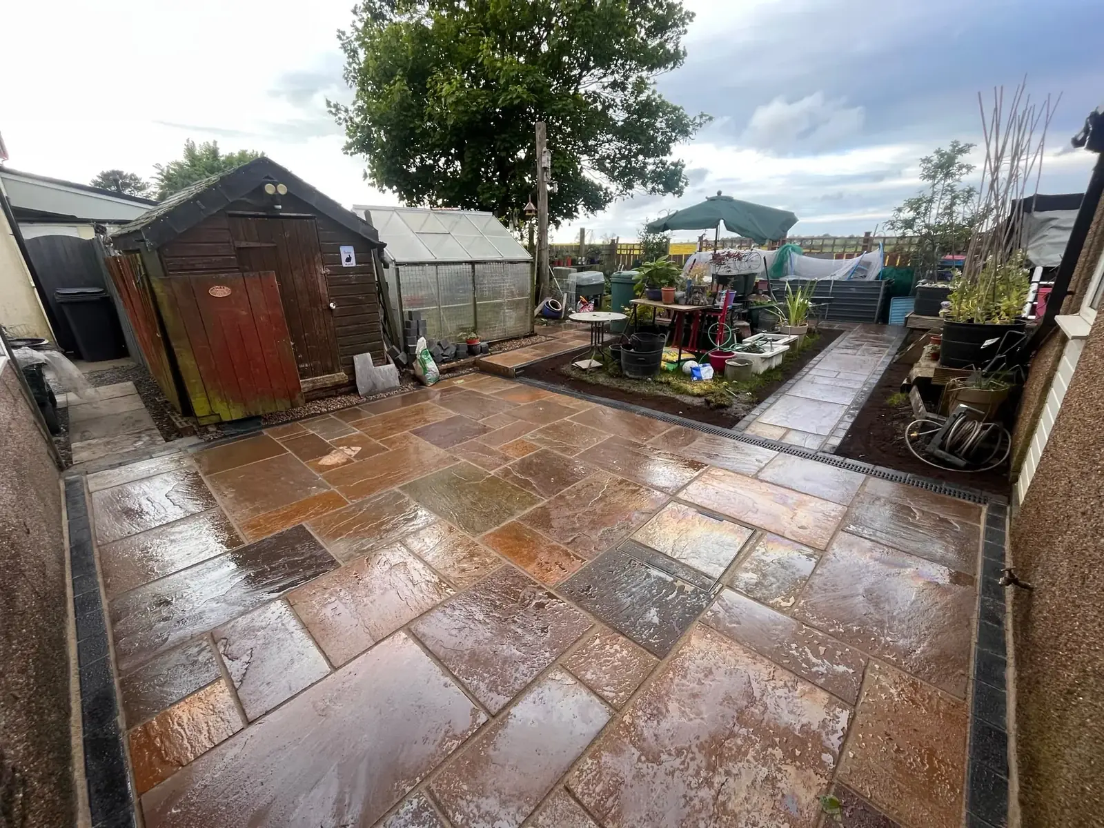 Completed sandstone patio with garden shed and greenhouse behind at a North East property